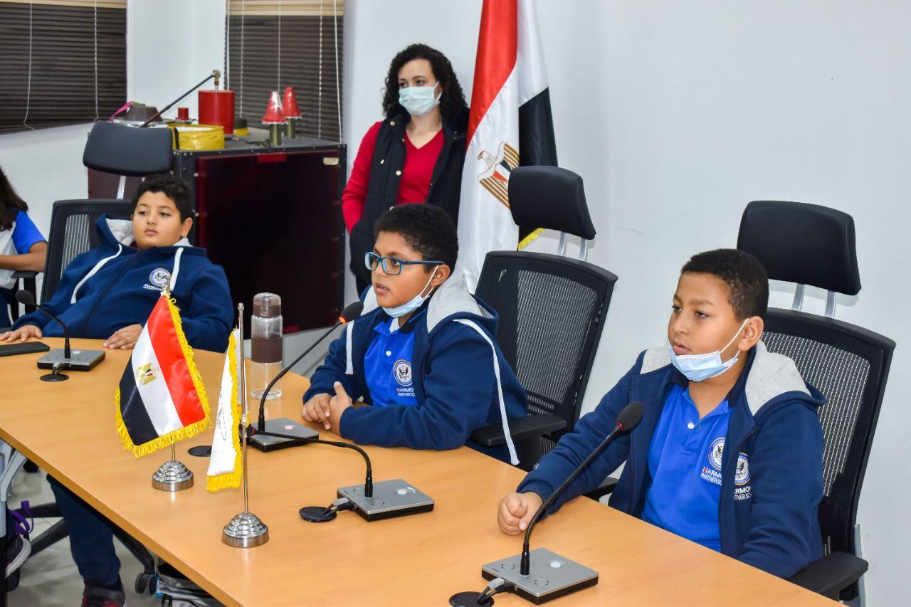 This image showcases young children from IVY STEM International School participating in a discussion or presentation. They are seated at a table equipped with microphones, wearing school uniforms and protective face masks. The presence of an Egyptian flag indicates the school's international focus. A teacher or facilitator can be seen in the background. This photo captures the interactive and engaging learning environment at IVY STEM International School.